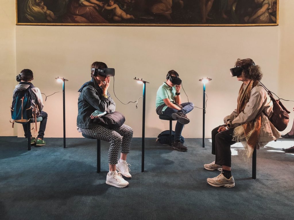 Vier Menschen sitzen in einer Kunstausstellung und tragen Virtual Reality Brillen.