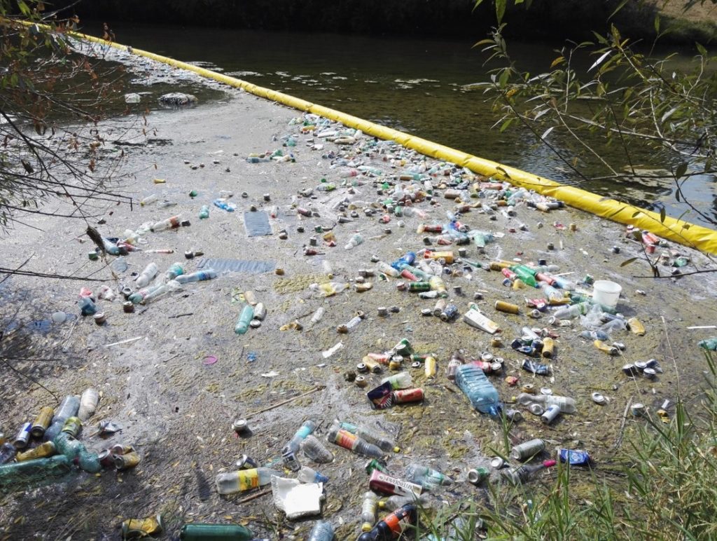 Eine gelbe Absperrung im Fluss hält eine Menge Müll davon ab, weiter zu fließen.