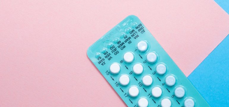 Eine türkise Packung der Anti-Baby-Pille auf rosa-blauem Grund.