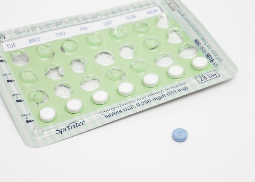 Eine fast leere, grüne Packung der Anti-Baby-Pille liegt auf weißem Grund, eine blaue Pille liegt daneben,