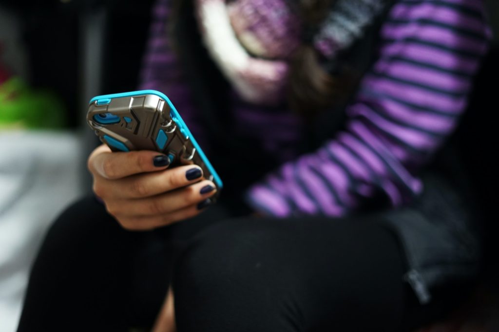 Eine Person mit dunkel lackierten Fingernägeln hält ein Smartphone. Das Gesicht der Person ist nicht zu sehen.