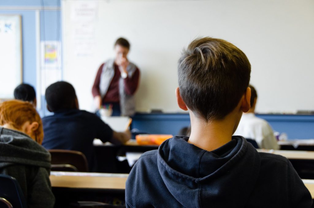 Das Bild zeigt einen Klassenraum aus der Sicht der Schüler*innen. Ein Kind in einem dunklen Pullover sitzt im Vordergrund.
