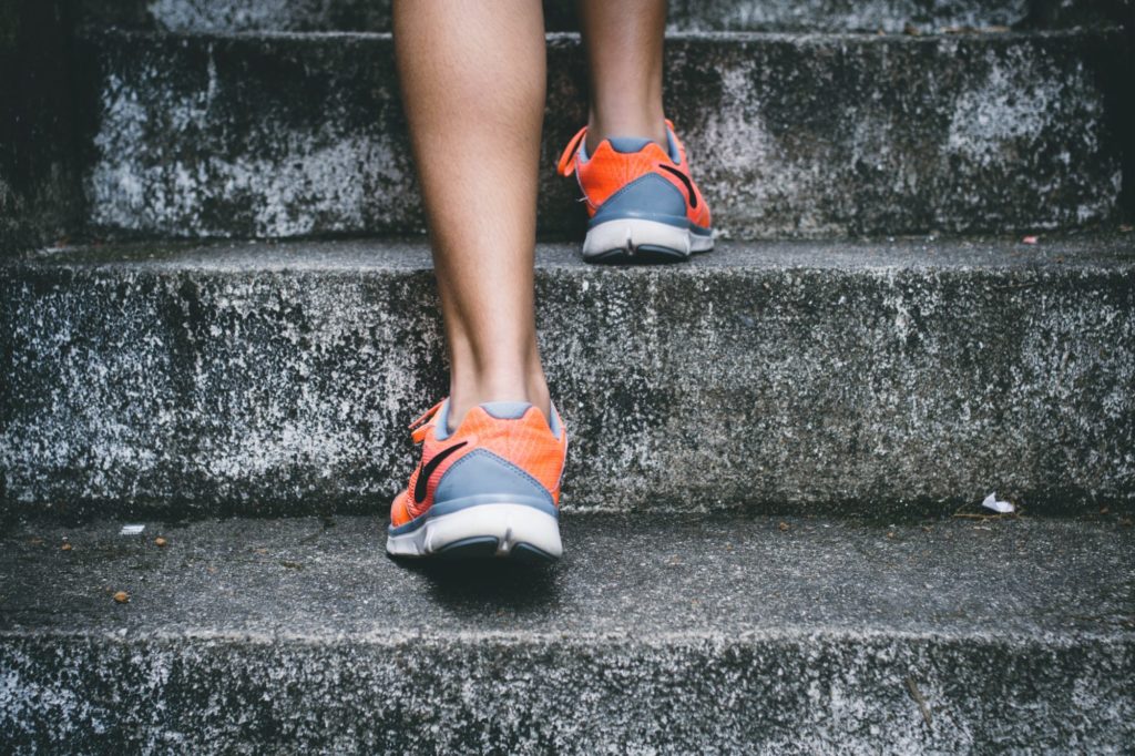 Das Bild zeigt zwei Füße einer Person in Laufschuhen, die eine Treppe hinauflaufen.