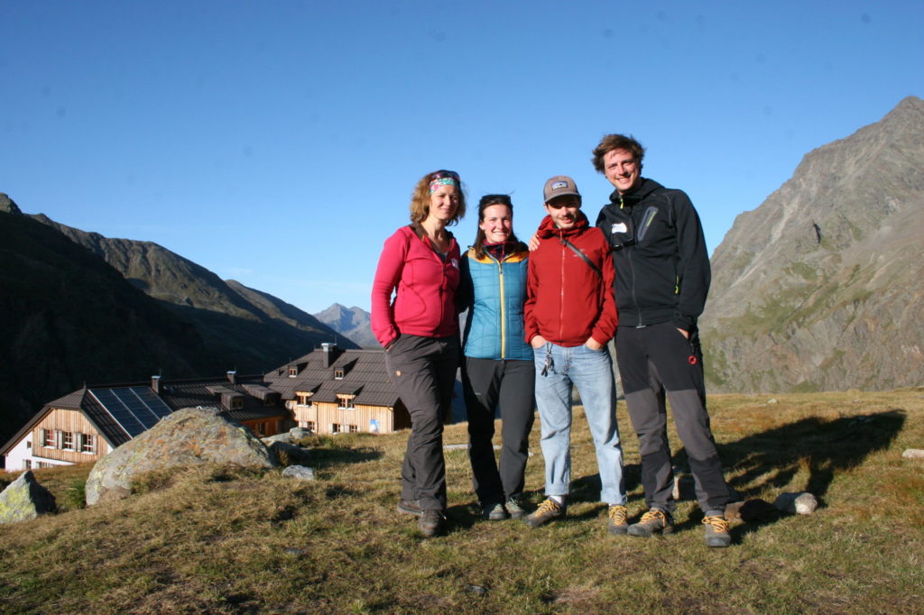 Das Forschungsteam der Uni Innsbruck (vier Personen) steht auf einem Hügel, im Hintergrund sieht man Berge und eine Hütte.