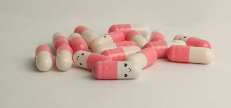 Das Bild zeigt rosa-weiße Pillen, auf die glückliche Gesichter gemalt wurden.