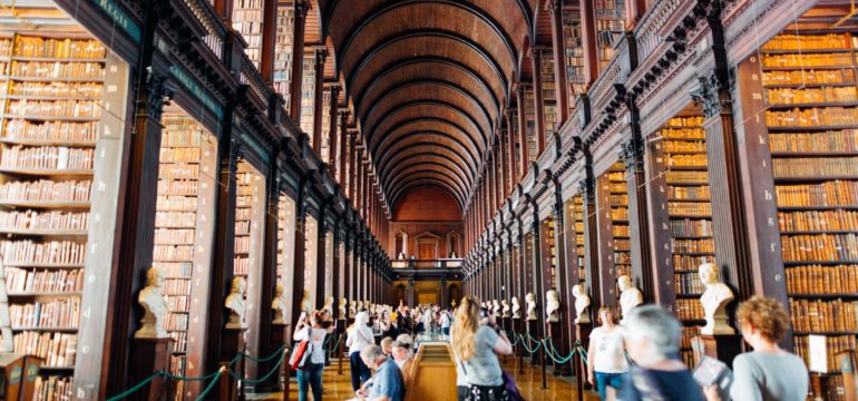 Das Foto zeigt die Bibliothek in Dublin. Man sieht viele Besucher*innen, die inmitten von dunklen Bücherregalen stehen.