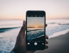 Eine Person hält ein Smartphone und fotografiert das Meer.