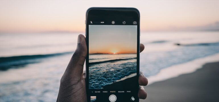 Eine Person hält ein Smartphone und fotografiert das Meer.
