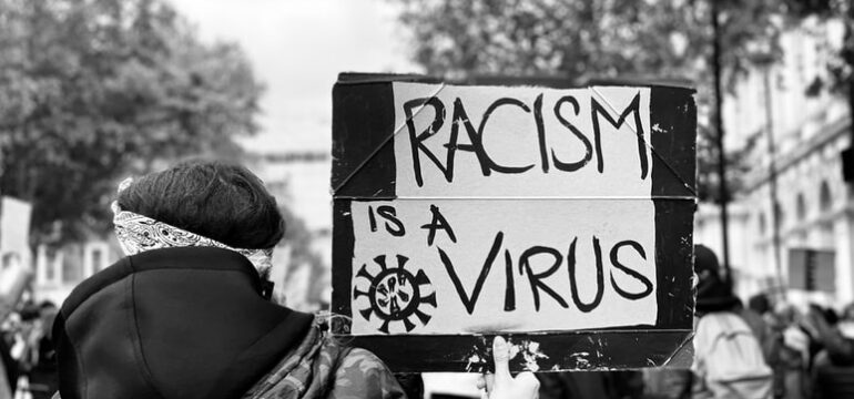 Eine Demonstrantin hält ein Schild mit der Aufschrift "Racism is a virus" hoch.