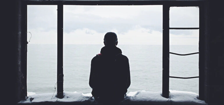 Ein Mann sitzt alleine vor dem offenen Meer.