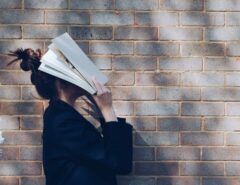 Eine Frau legt ein Buch gegen ihren Kopf.