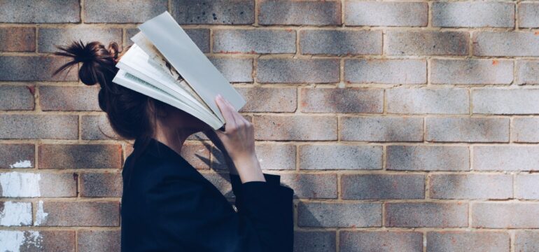 Eine Frau legt ein Buch gegen ihren Kopf.