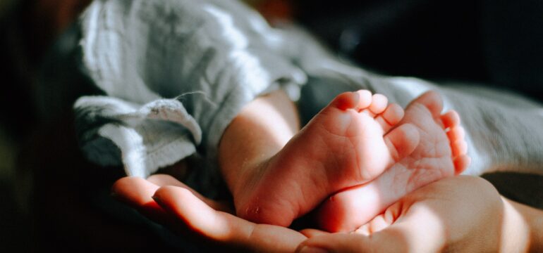 Eine erwachsene Person hält ein Baby, von diesem sind die Füße zu sehen.