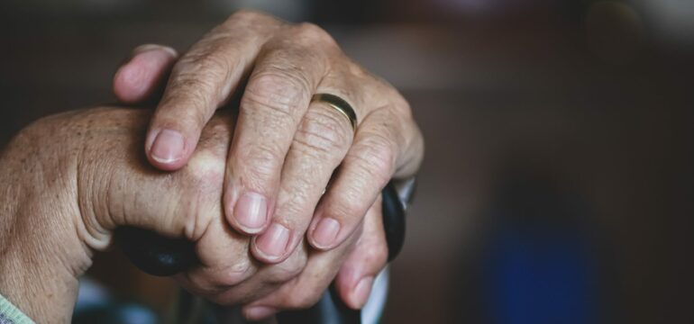 Die Hand einer älteren Person ist zu sehen, diese hält einen Gehstock.