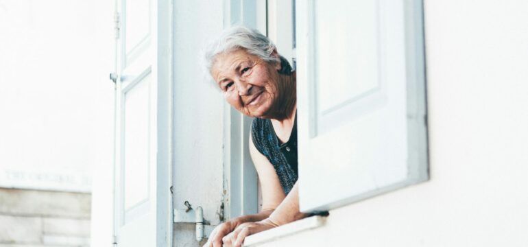 Eine ältere Frau schaut aus dem Fenster und lächelt.