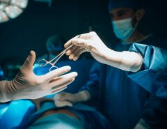 Zwei Personen sind im OP-Saal zu sehen, die eine reicht der anderen eine Schere.