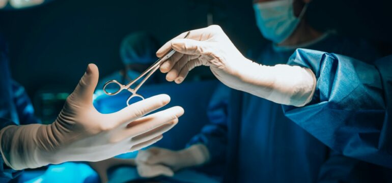 Zwei Personen sind im OP-Saal zu sehen, die eine reicht der anderen eine Schere.