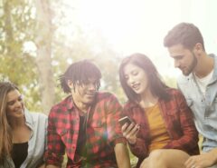 Einige junge Menschen sitzen gemeinsam zusammen und schauen auf ein Smartphone.