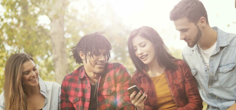 Einige junge Menschen sitzen gemeinsam zusammen und schauen auf ein Smartphone.