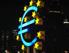 Ein riesiges Euro-Zeichen und Sterne, im Hintergrund Gebäude.