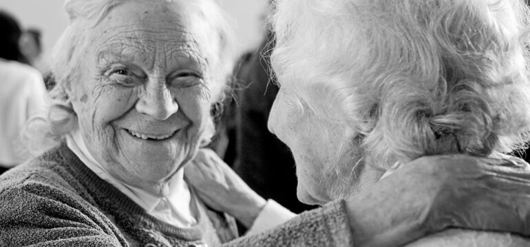 Zwei ältere Frauen lächeln einander an.